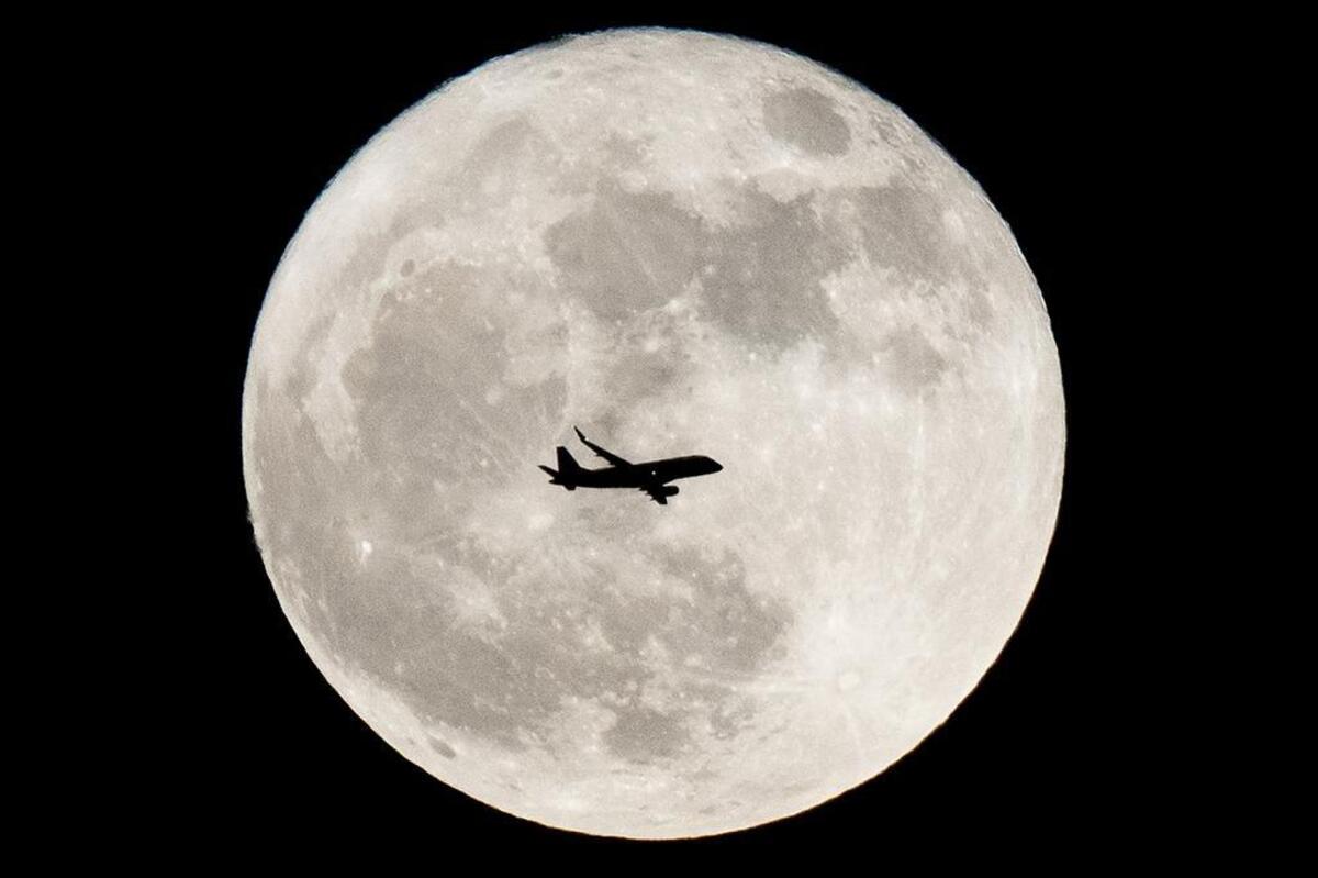 An airplane travels across a full moon.